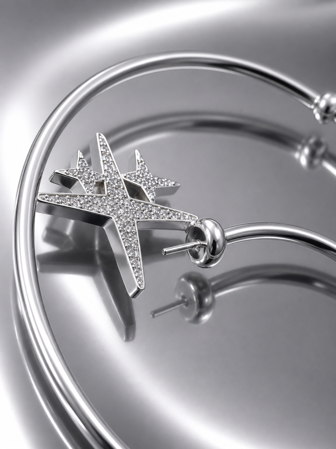 Near Earth Object | Silver star-shaped earring on a reflective surface