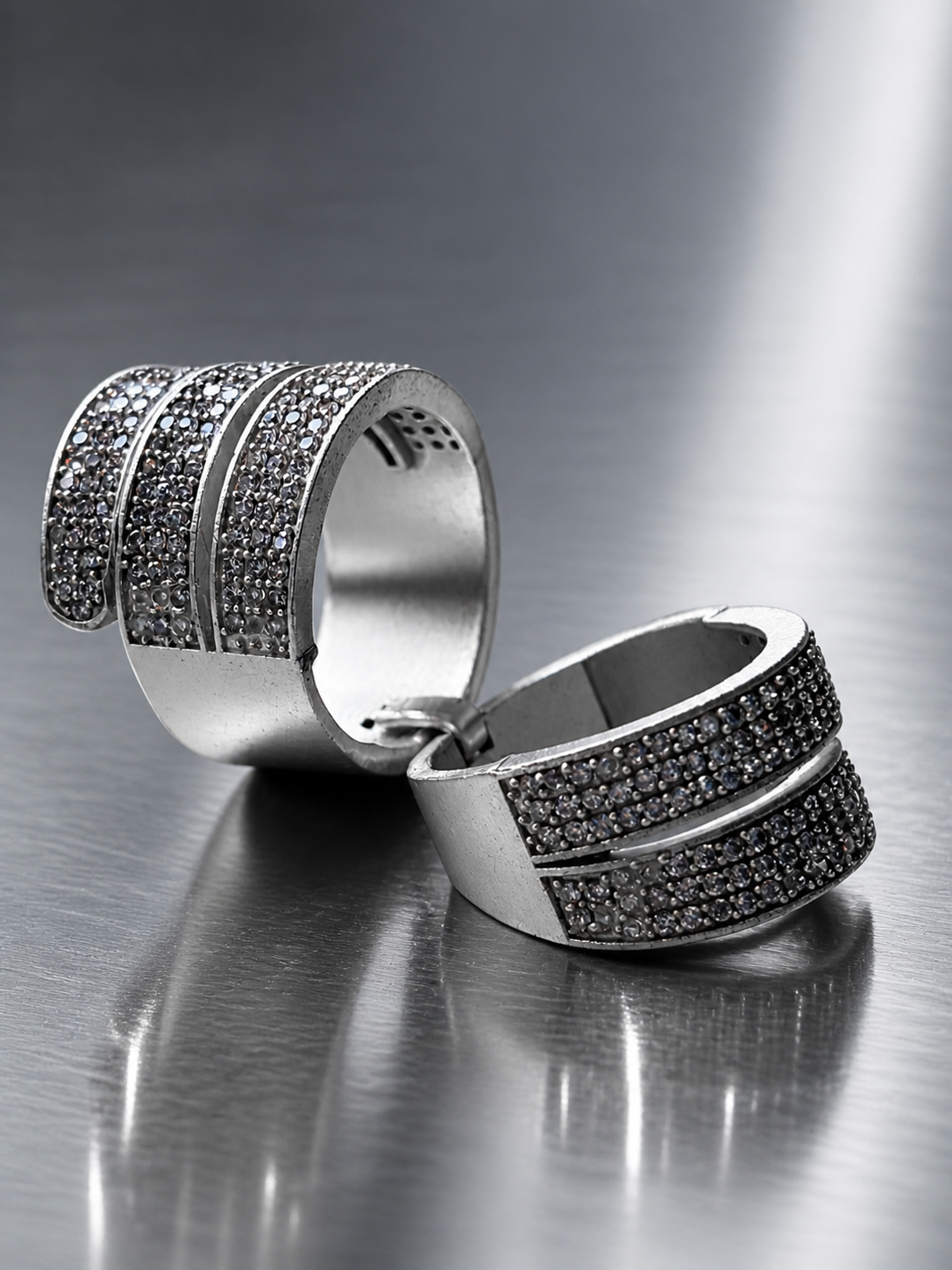 Pair of silver rings with black gemstones on a reflective surface