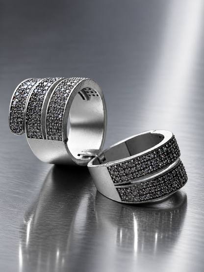 Pair of silver rings with black gemstones on a reflective surface