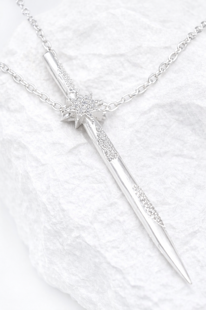 Near Earth Object | Silver sword-shaped necklace with star details on a white fabric background