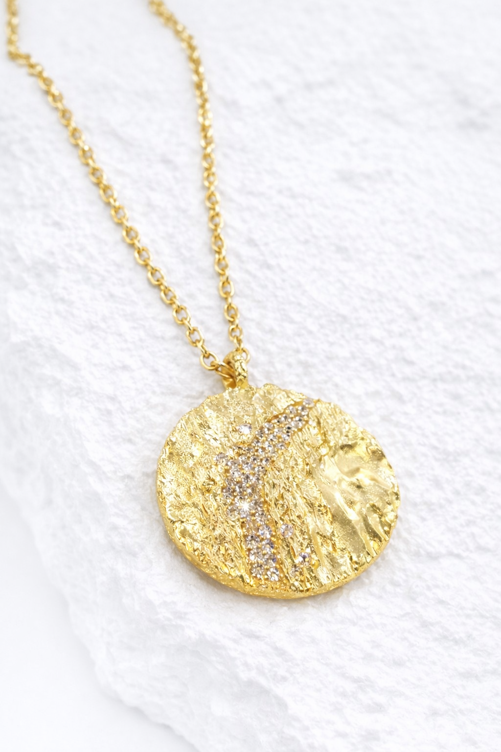 Near Earth Object | Gold necklace with a textured pendant on a white background
