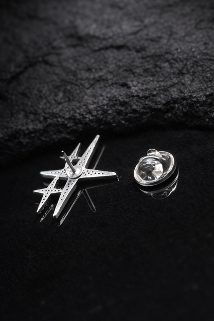 Near Earth Object | Star-shaped silver pin and round silver brooch on a dark textured surface