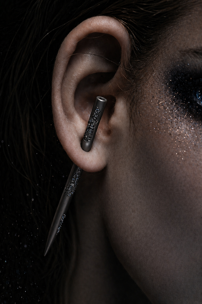 Near Earth Object | Close-up of an ear with a dark metallic earring against a dark background