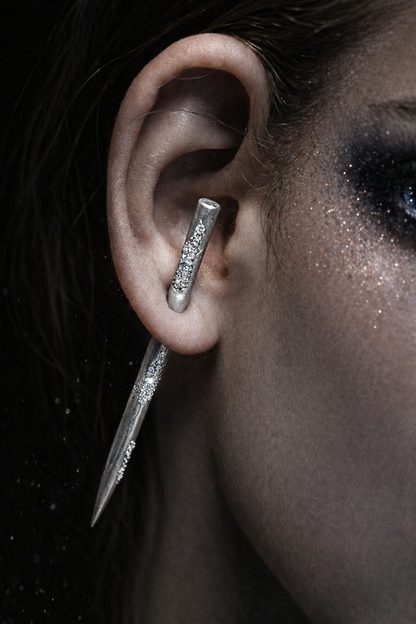 Near Earth Object | Close-up of an ear with a unique earring design against a dark background