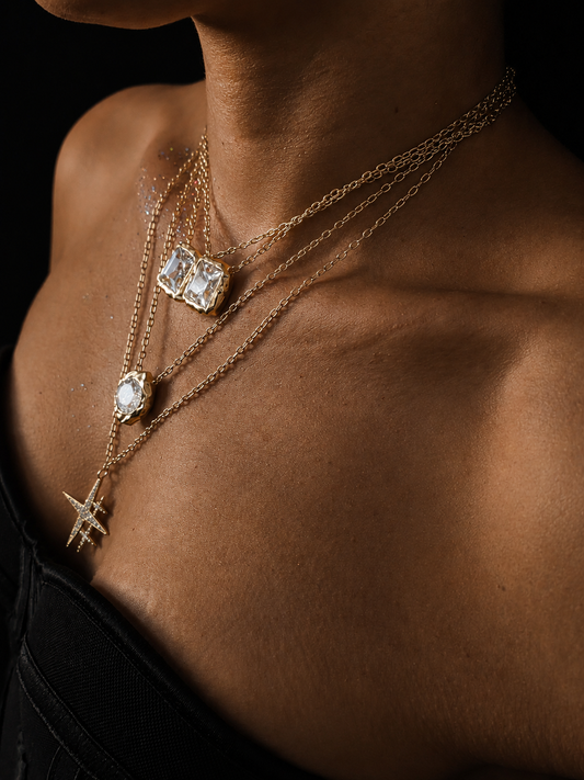 Near Earth Object | Close-up of a person wearing multiple gold necklaces with gemstone pendants on a dark background