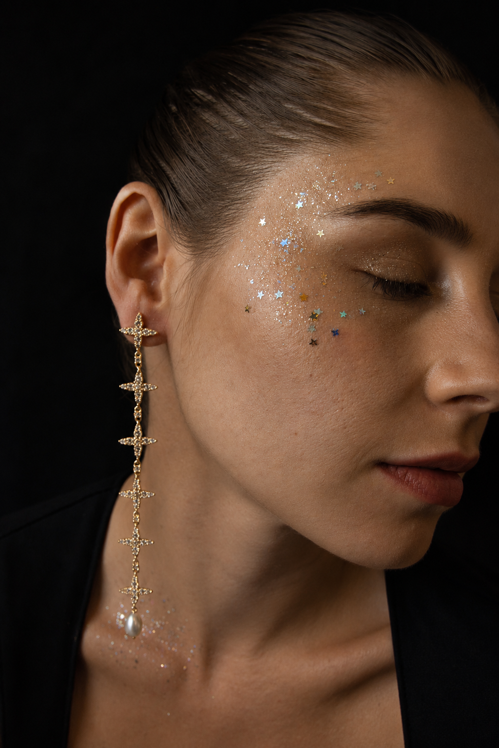 Near Earth Object | Close-up of a woman's face with glitter on her face, wearing a long dangling earring.
