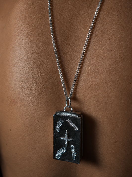 Near Earth Object | Silver necklace with a rectangular pendant on a person's neck against a brown background
