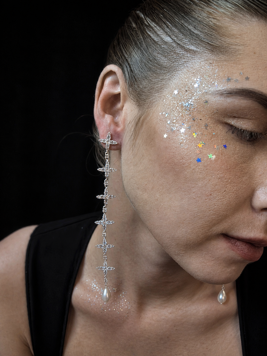 Near Earth Object | Close-up of a woman wearing a long, dangling earring with a black background