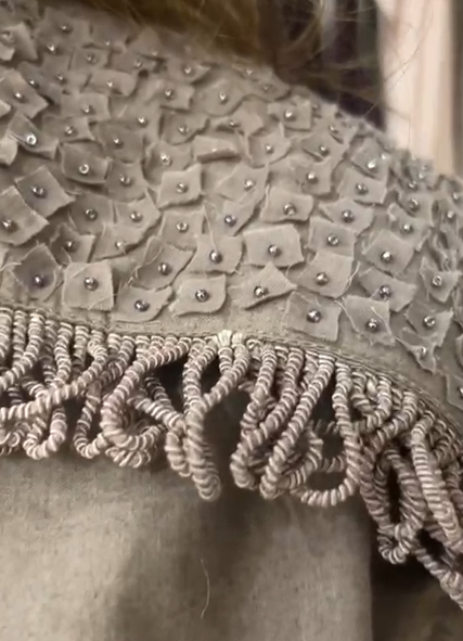 Crater Matter Set : Close-up of intricate fabric detailing on a taupe Top, featuring textured square appliqué with small metallic bead embellishments and decorative knotted fringe trim, handcrafted appliqué fabric with silver bead embellishment. | Women's Top | Pret Clothes | Asymmetrical Top | nEo Clothes