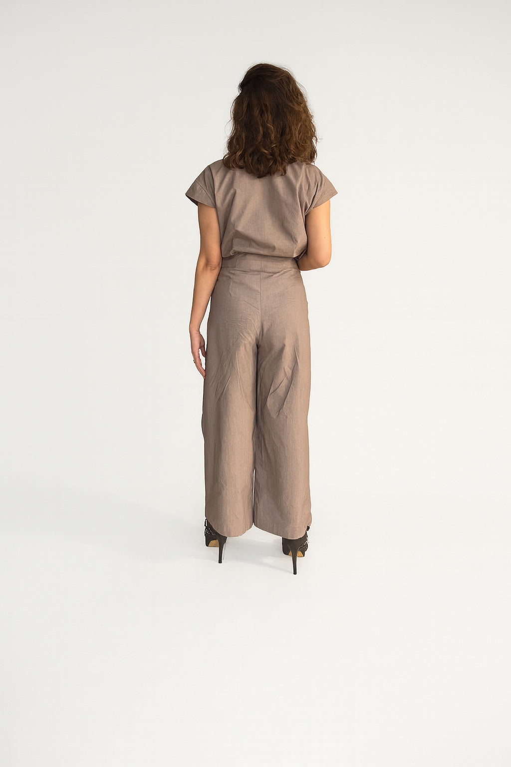 Crater Matter Set : Back view of a woman wearing a taupe draped Top with short sleeves and wide-leg silhouette, styled with black stiletto heels - near Earth object | Women's Top | Pret Clothes | Asymmetrical Top | nEo Pant