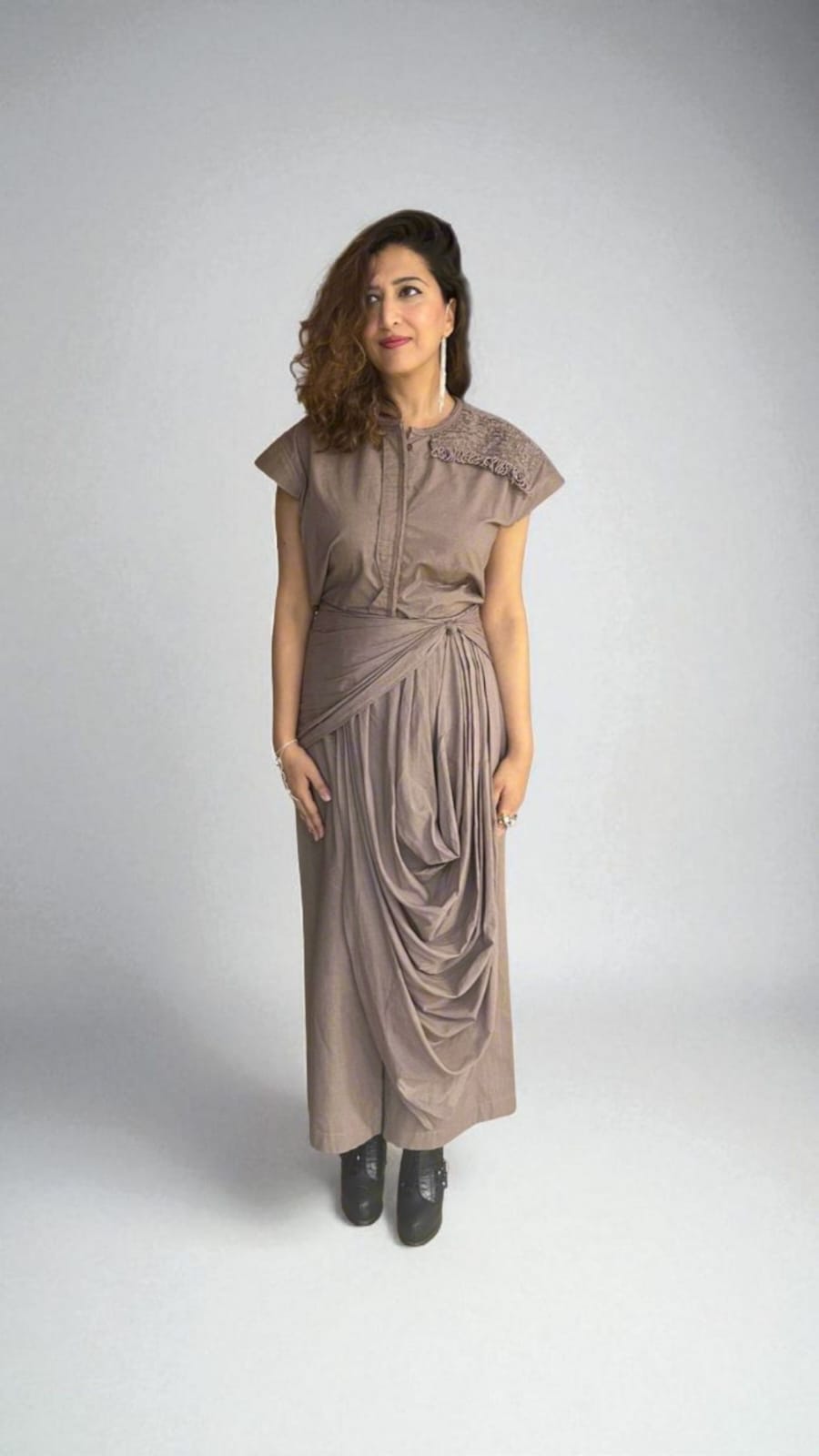 Crater Matter Top : A woman wearing a taupe draped Top with cap sleeves and intricate shoulder detail, styled with gathered pleats at the waist and a cascading draped Pant. She pairs the outfit with black ankle boots, minimal jewelry. women’s contemporary drape  Top for evening wear - near Earth object | Women's  Top | Pret Clothes | Asymmetrical Top | nEo Clothes 