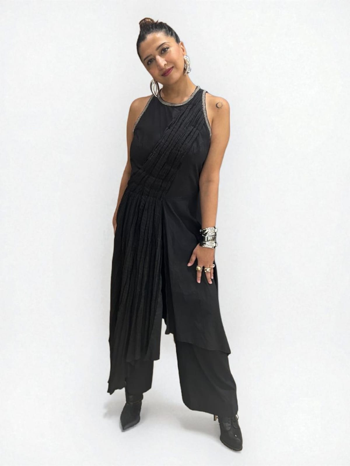 Moon Crescent Jumpsuit : Women wearing a modern black asymmetrical Jumpsuit with pleated detailing,  a sleeveless design with metallic edging at the neckline. Accessorizes with bold silver jewelry including hand cuff, stacked rings, and hoop earrings, The overall style is a fusion of contemporary and ethnic fashion, giving off a confident, Trendy sleeveless Jumpsuit outfit for women with ethnic silver jewelry - near Earth object | Women's Jumpsuit | Pret Clothes | Asymmetrical Jumpsuit | nEo clothes