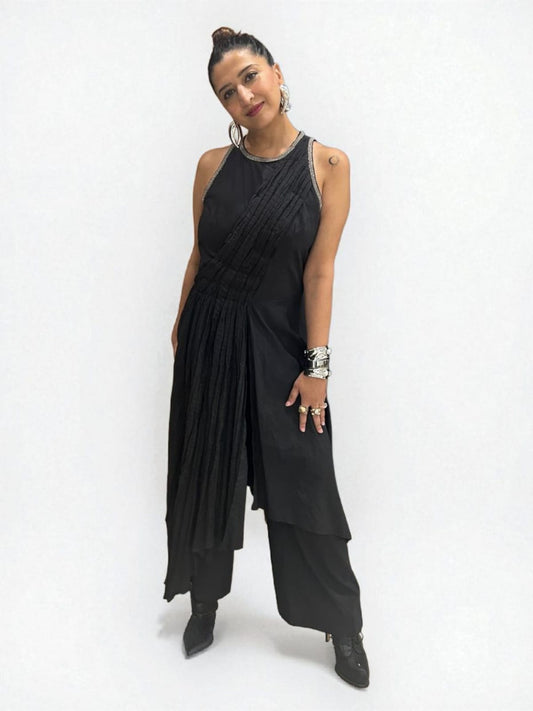Moon Crescent Jumpsuit : Women wearing a modern black asymmetrical Jumpsuit with pleated detailing,  a sleeveless design with metallic edging at the neckline. Accessorizes with bold silver jewelry including hand cuff, stacked rings, and hoop earrings, The overall style is a fusion of contemporary and ethnic fashion, giving off a confident, Trendy sleeveless Jumpsuit outfit for women with ethnic silver jewelry - near Earth object | Women's Jumpsuit | Pret Clothes | Asymmetrical Jumpsuit | nEo clothes