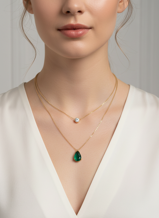 Model wearing layered gold necklace with pear-cut emerald pendant styled with a deep V-neck – refined gemstone jewellery by Near Earth Object.
