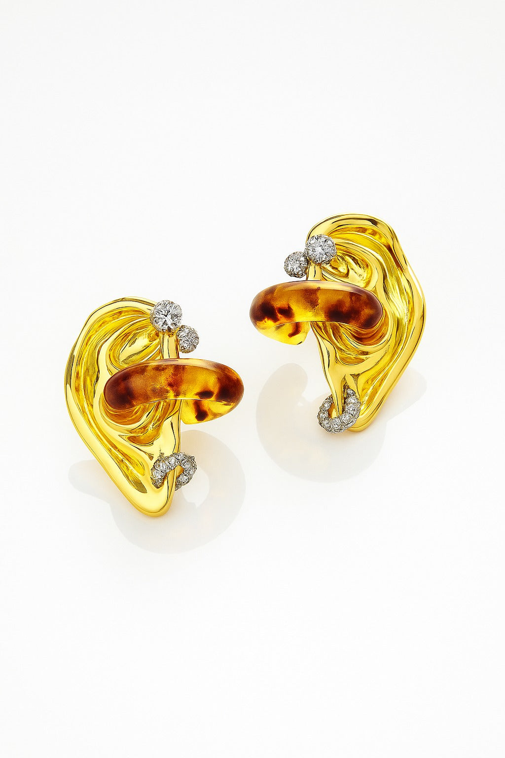 Abstract sculptural gold earrings with amber-toned resin loops and sparkling crystal accents on a white background.
