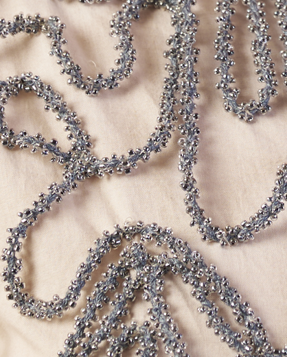 Close-up of decorative silver tinsel on a textured beige surface  | Women Dresses | Pret Clothes | nEo Clothes.