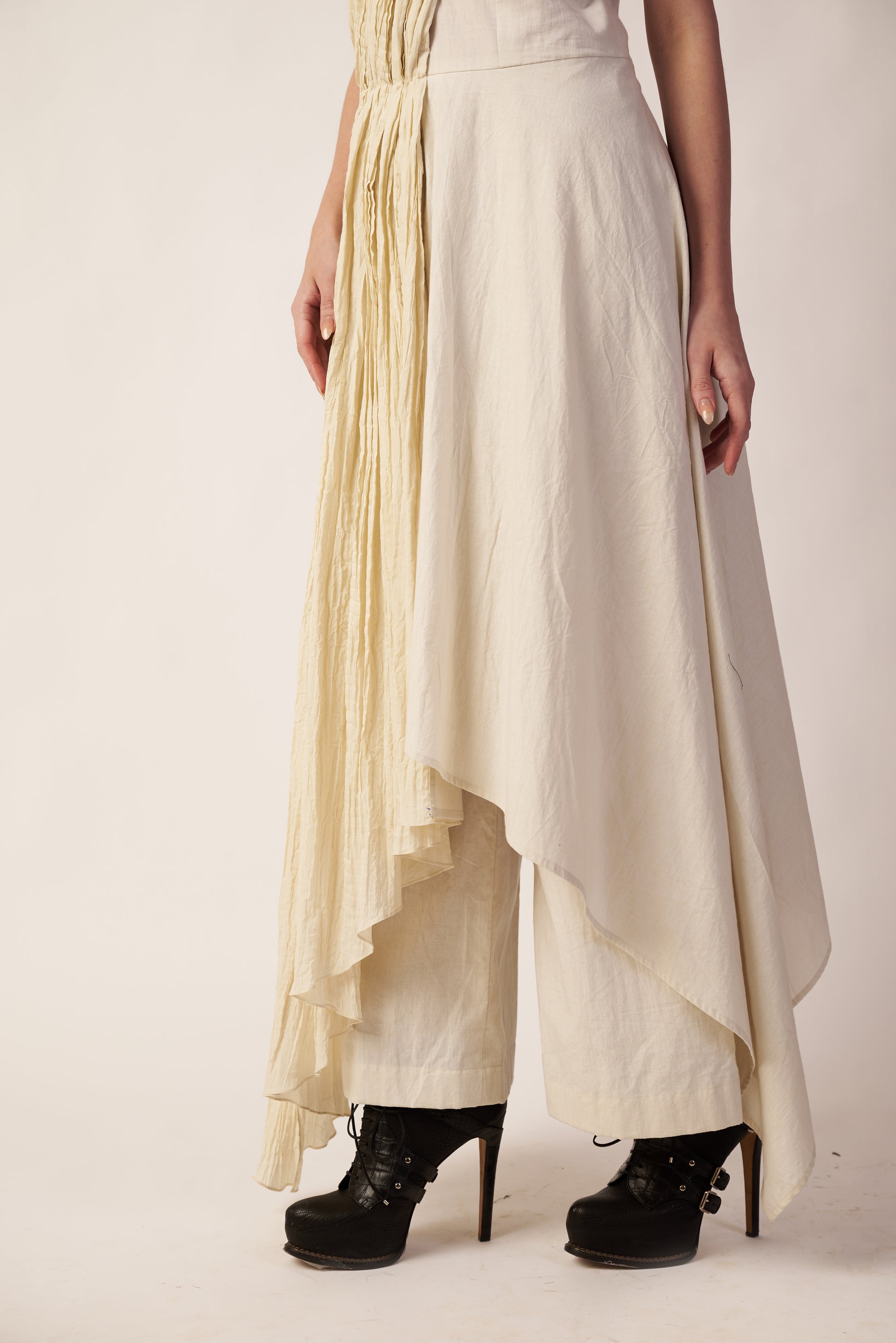 Person wearing a long, light-colored dress with a high-low hemline and black high-heeled shoes | Women Jumpsuit | Pret Clothes | nEo Clothes.