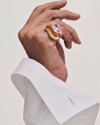 Near Earth Object | Hand wearing a gold ring with a pink gemstone on a light background