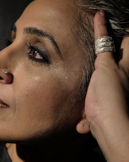 Near Earth Object | Close-up of a person with glitter on their face and hand wearing a ring.