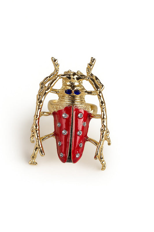 Bold gold ring shaped like a sculptural beetle with red enamel wings, black detailing, and crystal accents.