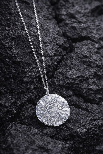 Near Earth Object | Silver necklace with a round pendant on a dark textured surface