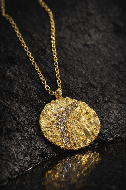 Near Earth Object | Gold necklace with a textured pendant on a dark surface