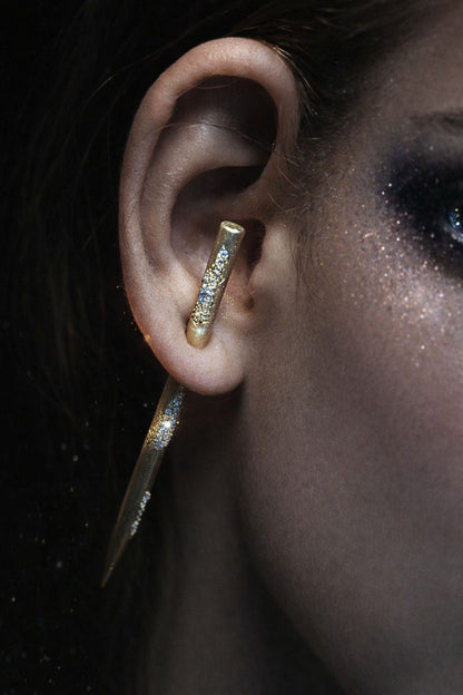 Near Earth Object | Close-up of a person wearing gold hoop earrings with a dark background