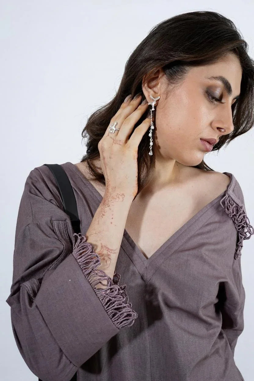 Woman wearing a Beige dress with fringe details, She accessorizes with statement silver jewelry, including a long dangling earring and silver rings. modern women’s jumpsuit outfit with minimal style and bold accessories  | Women Jumpsuit | Pret Clothes | nEo Clothes.