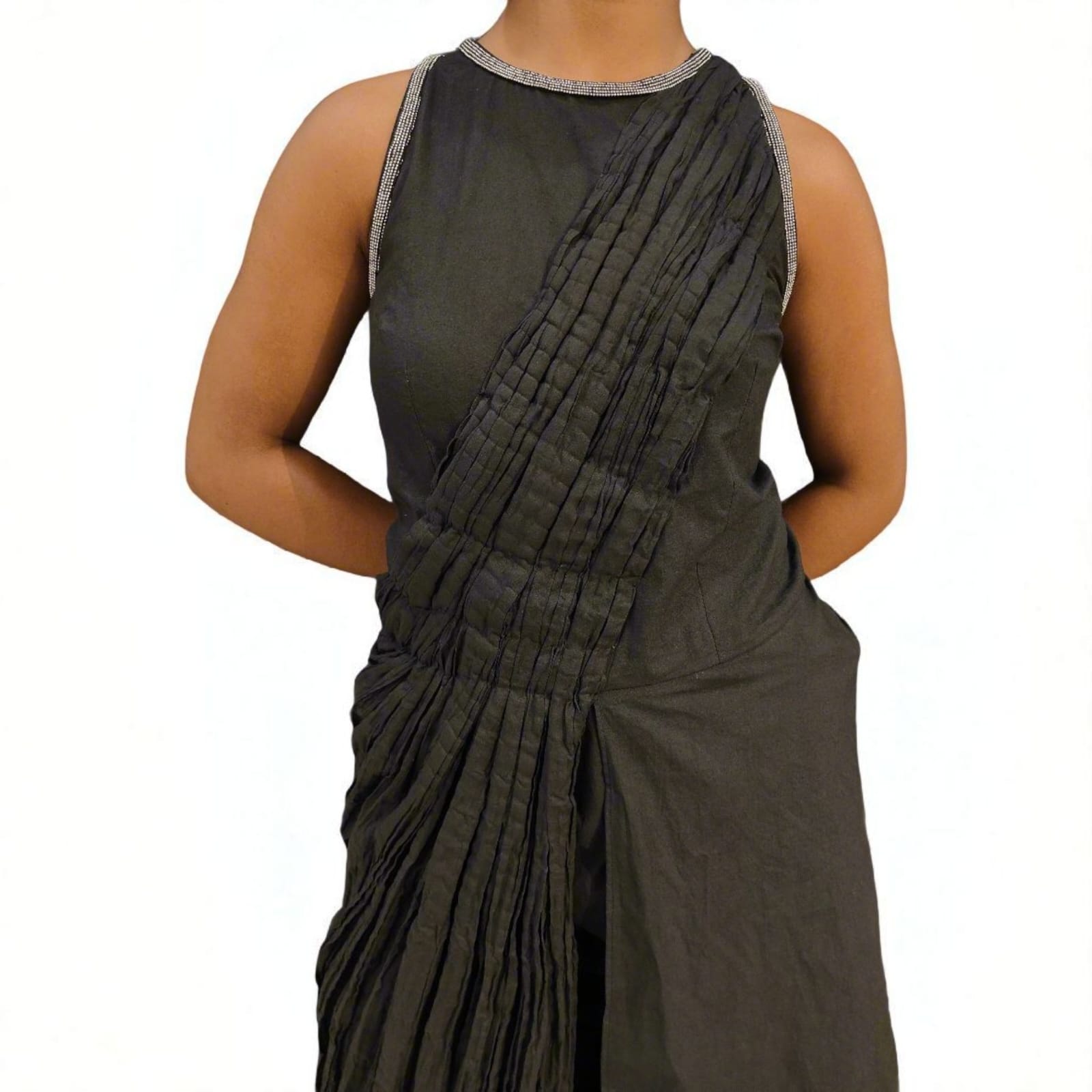 A close-up view of a sleeveless black asymmetrical jumpsuit featuring pleated detailing running diagonally across the front, The neckline is round with a metallic silver trim, adding a subtle accent to the otherwise minimalist design, Women’s designer jumpsuit with structured pleated front panel.| Women's jumpsuit | Pret Clothes | Asymmetrical jumpsuit | nEo Clothes