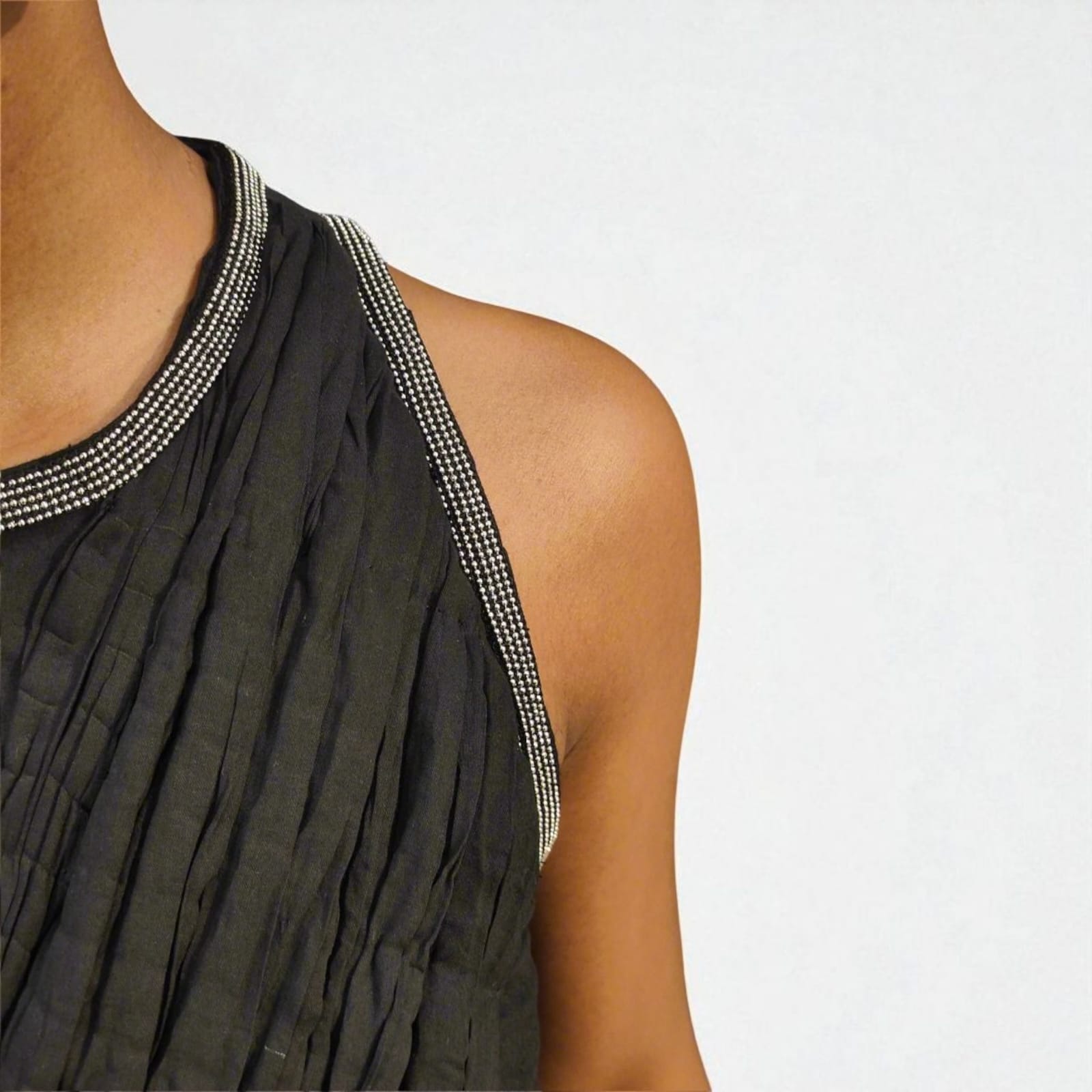 A close-up detail shot of a black sleeveless Jumpsuit, focusing on the neckline and shoulder, with intricate metallic silver beaded trim, adding a refined contrast against the matte black pleated fabric, emphasizes fabric quality, stitching, and embellishment details. | Women's Jumpsuit | Pret Clothes | Asymmetrical Jumpsuit| nEo Clothes