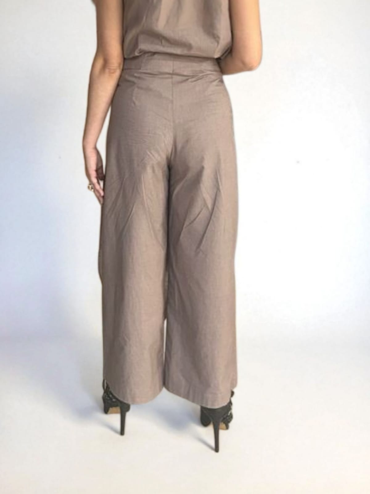 Back view of a woman wearing a taupe draped Pant with short sleeves and wide-leg silhouette, styled with black stiletto heels | Women's Pant | Pret Clothes | Asymmetrical Pant | nEo Pant