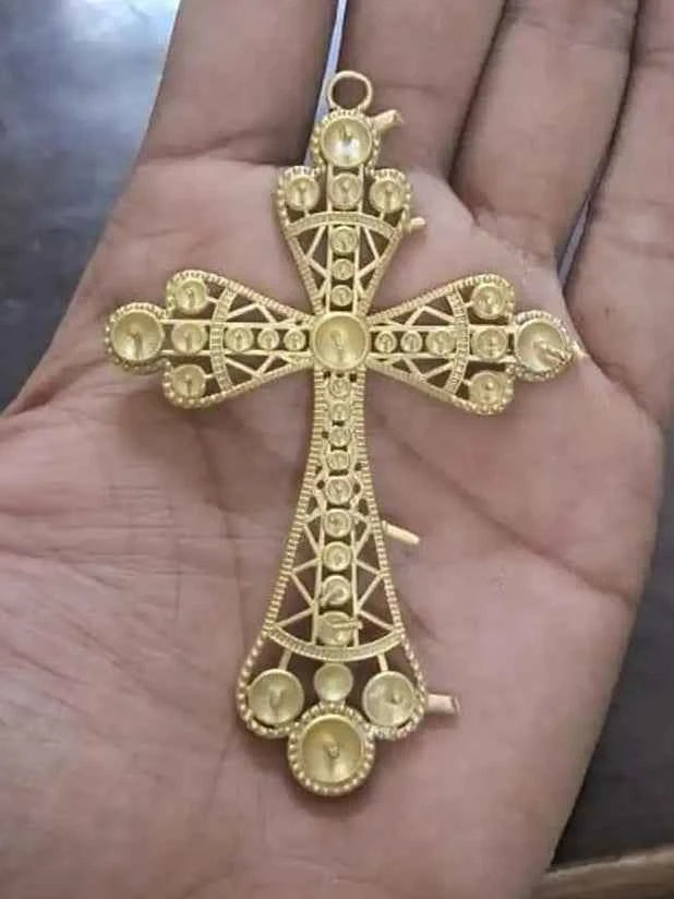 Gold cross pendant held in a hand on a wooden surface