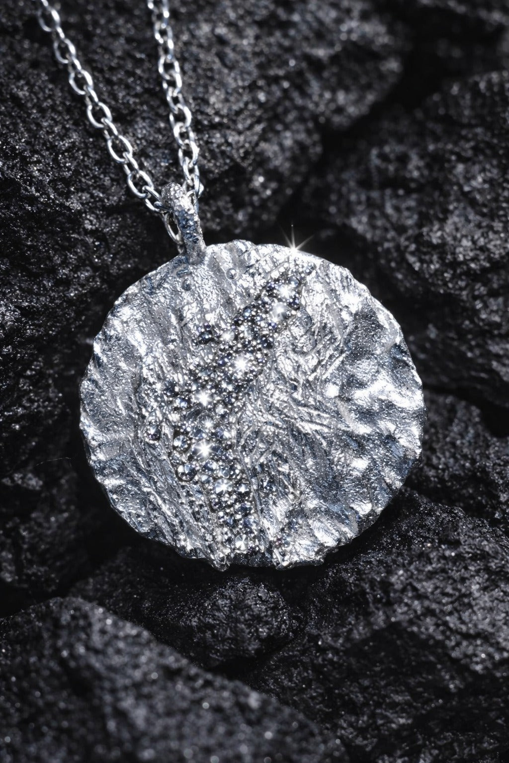 Near Earth Object | Silver textured pendant necklace on a dark stone surface