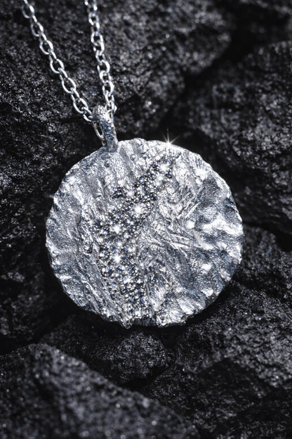 Near Earth Object | Silver textured pendant necklace on a dark stone surface