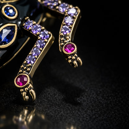 Near Earth Object | Decorative brooch with gold detailing, purple and red gemstones on a dark background